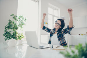 Profile side view photo of beautiful cute youth sit desk table raise fists scream shout yeah eyewear eyeglasses light apartment wear checkered shirt plaid goal celebration Auto-Accident-Doctor-Utah-NearSLC